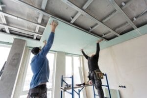 Workers hanging and finishing drywall panel into frame of ceiling. replace your drywall